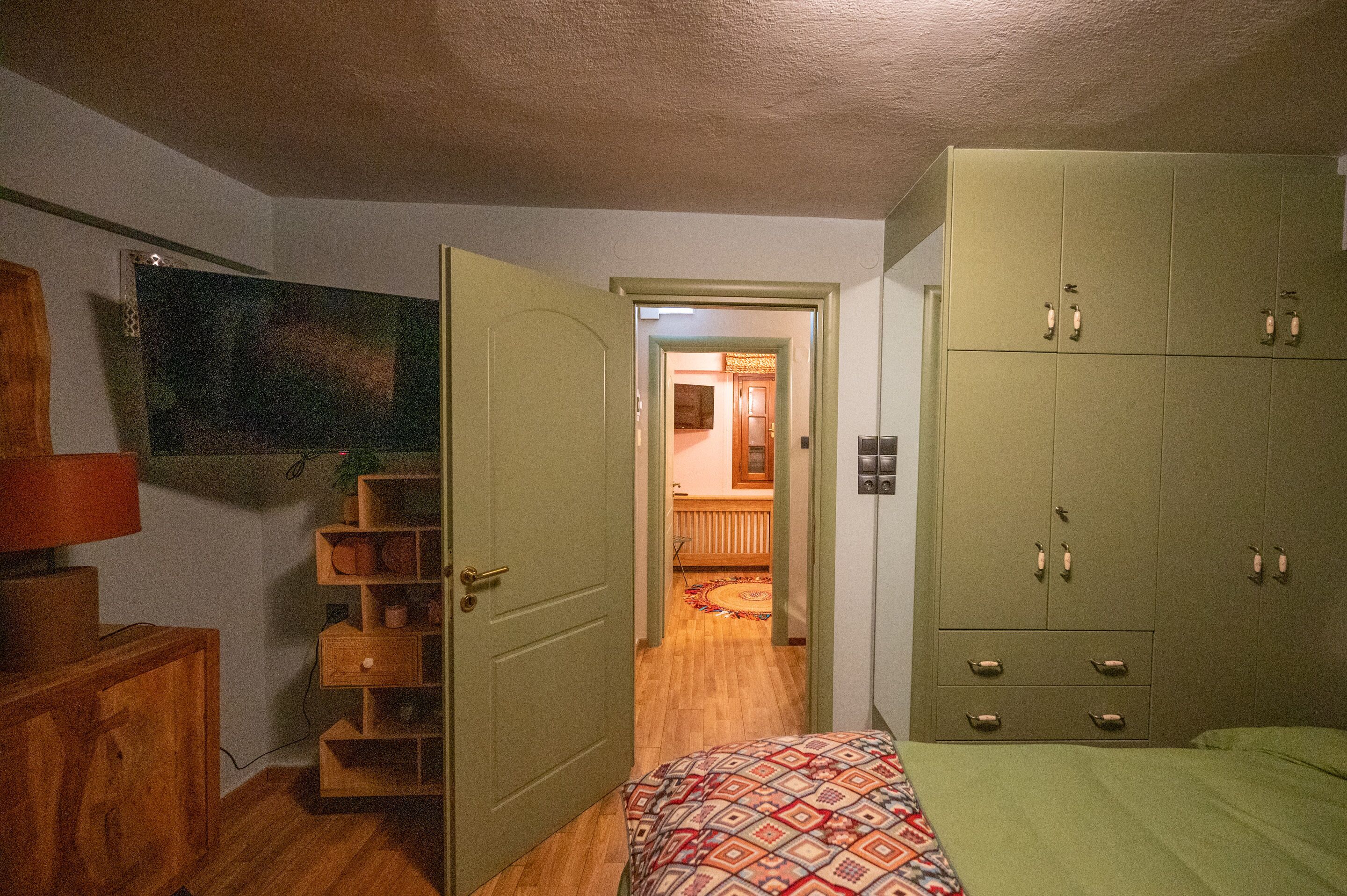 Une chambre à coucher comprenant un lit, une armoire, un téléviseur et une porte donnant sur une autre pièce.