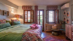 A bedroom with a bed, a bedside table, a lamp, a window with curtains, a radiator, and a wall-mounted air conditioner. - Dandy Villas Ioannina- Colorful Boutique House (Ioannina)