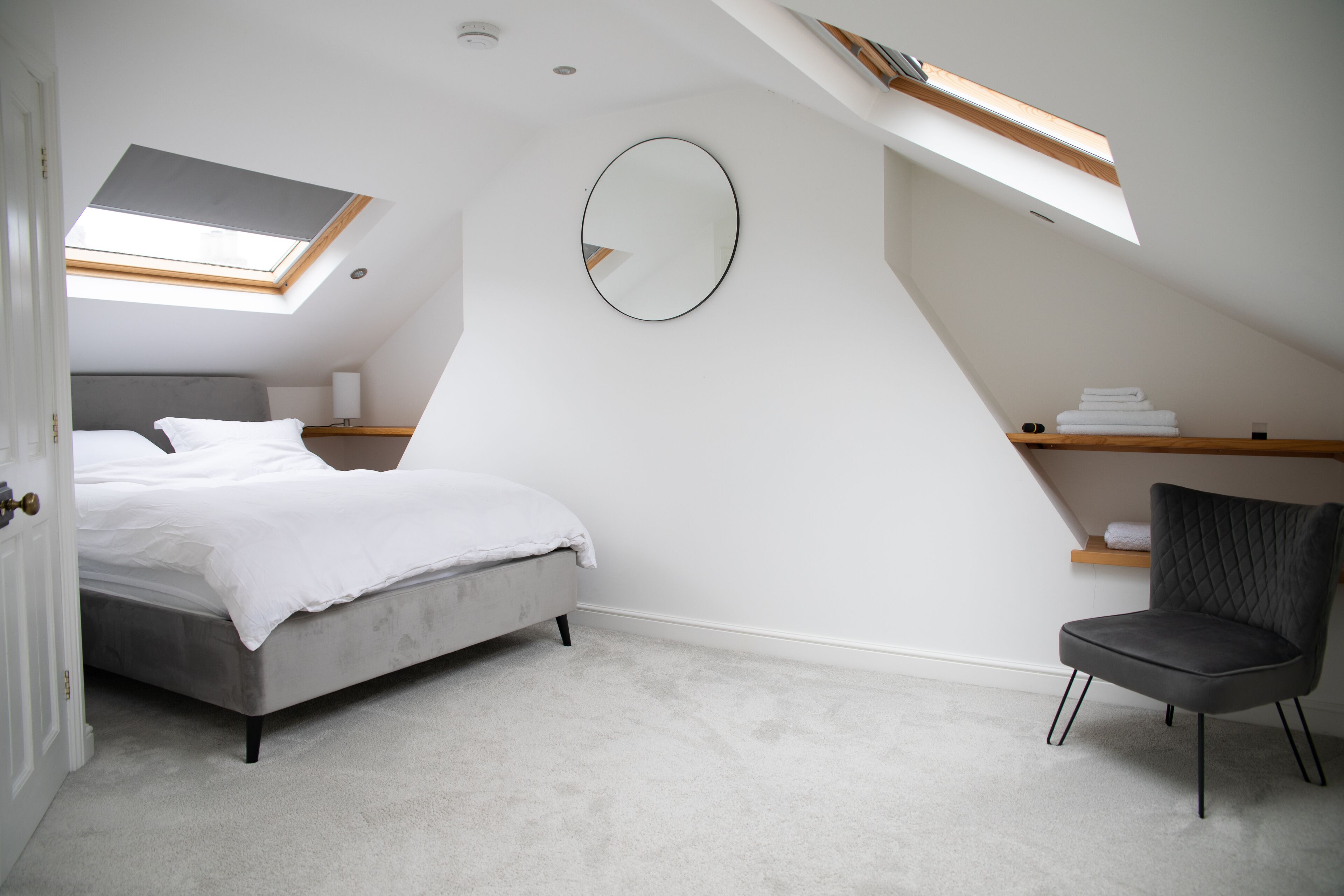 Une chambre à coucher avec un lit, une chaise, un miroir rond et une lucarne.