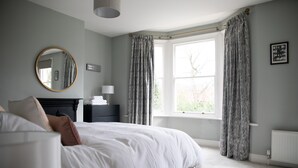 A bedroom with a large bed, a bedside table, a mirror, and a window with curtains. - York Minster-3 Bed-sleeps 6-fireplace-free Parking (York)