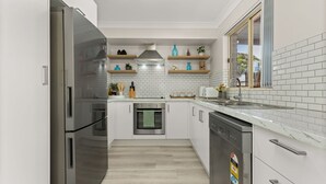 A modern kitchen with stainless steel appliances, white tiled backsplash, wooden shelves, and a window with a view.
