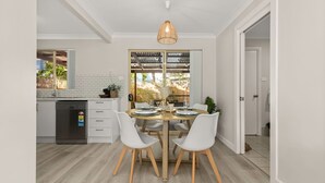 A modern kitchen with white cabinetry, a built-in dishwasher, and a dining area with a round wooden table and white chairs.