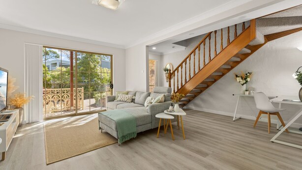 A spacious living room with a large sectional sofa, a wooden staircase, and a view of the outdoors.