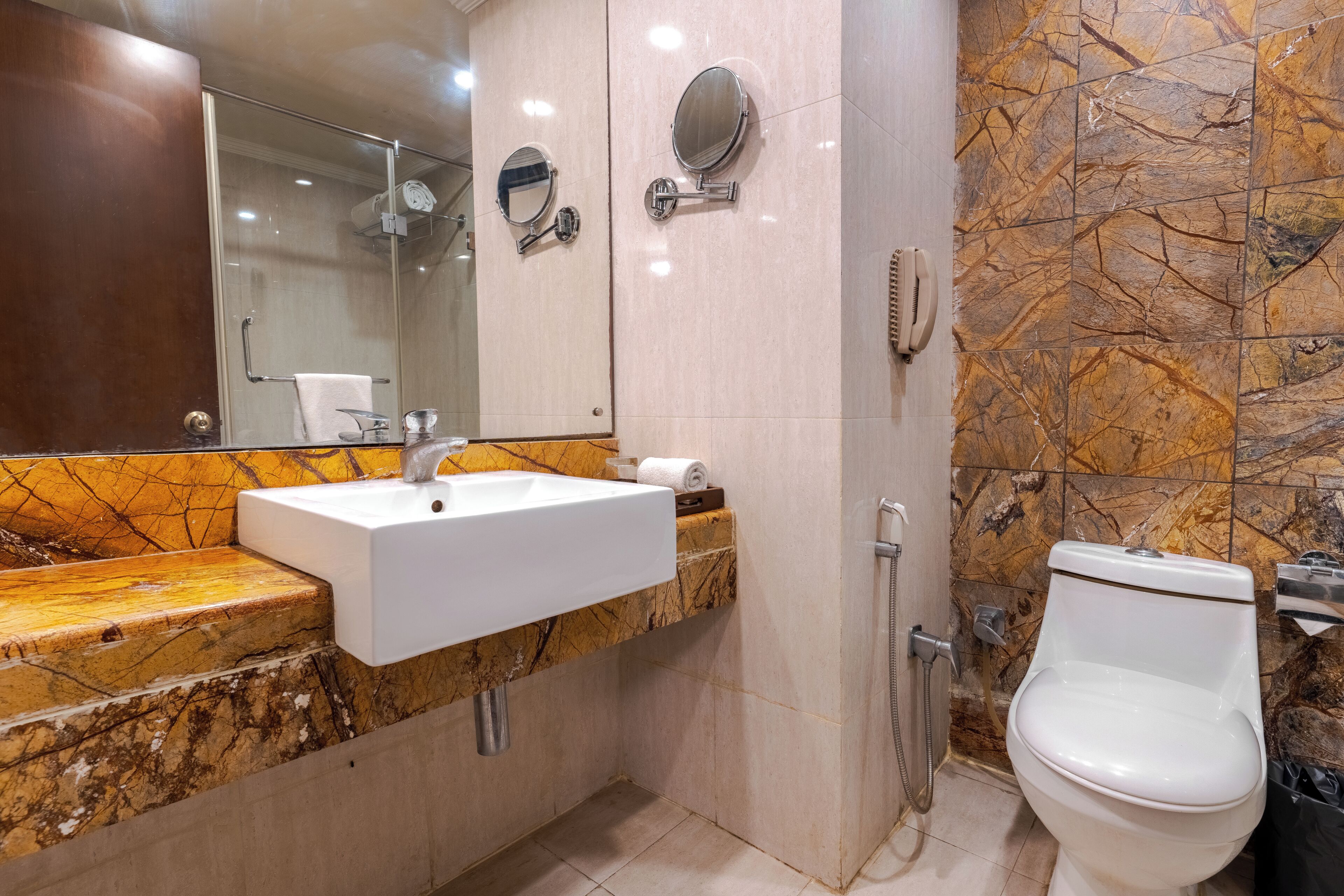 A bathroom with a marble sink, a toilet, a shower, and a mirror.