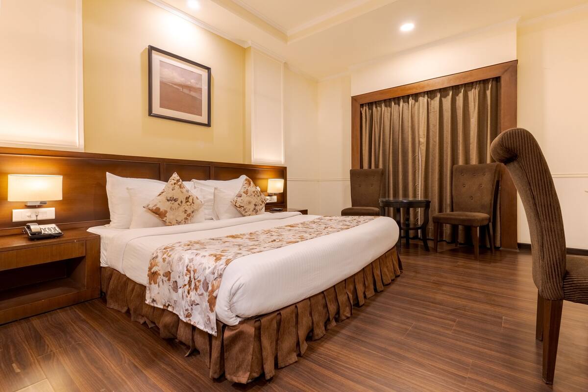 A hotel room with a large bed, bedside lamps, a chair, a small table, and a curtain.