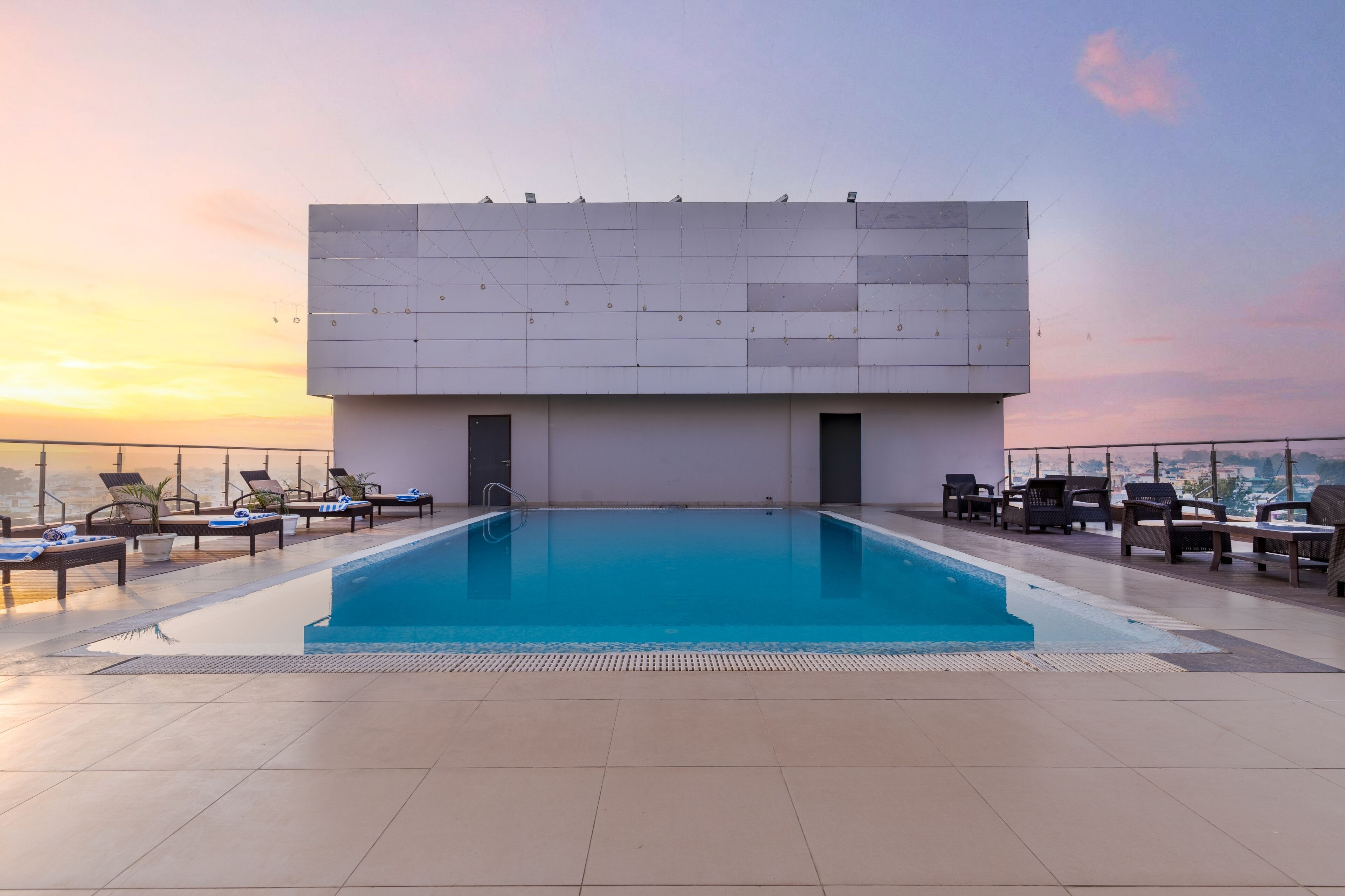 Una piscina en la azotea con sillones de descanso y vistas a la ciudad al atardecer.