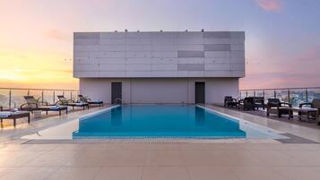 Une piscine sur le toit, avec des chaises longues et une vue sur la ville au coucher du soleil.