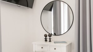 Un baño con tocador blanco, espejo redondo, televisor de pantalla plana y cortina gris.