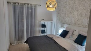 Ein Schlafzimmer mit Bett, Kleiderschrank, Deckenleuchte und einem Fenster mit Vorhängen.