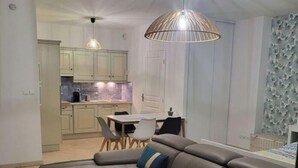 Ein modernes Wohnzimmer mit einem Ecksofa, zwei weißen Couchtischen und einem Essbereich mit Tisch und Stühlen.