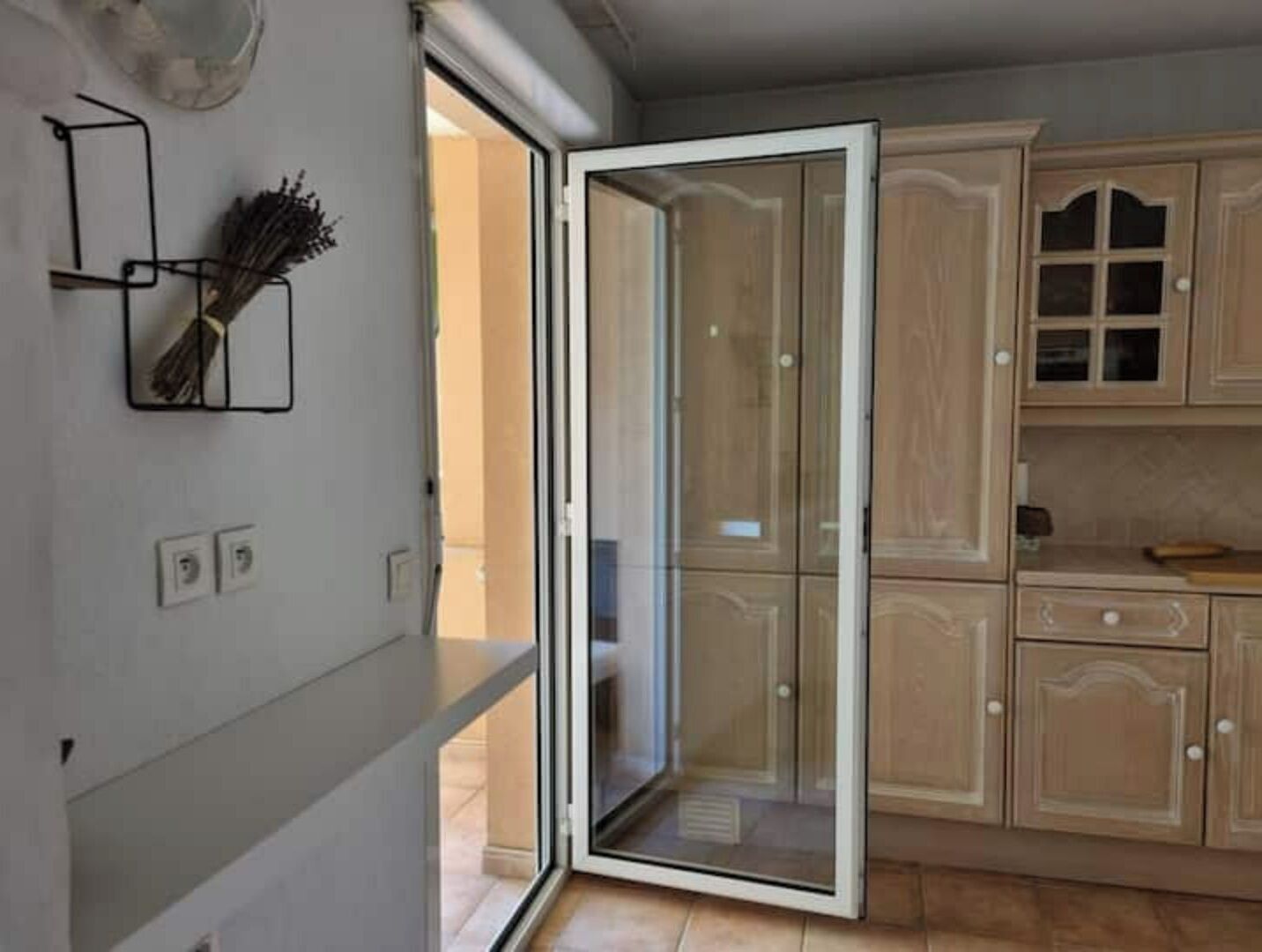 Een keuken met houten kastjes, een schuifdeur met glas en een wandlamp.