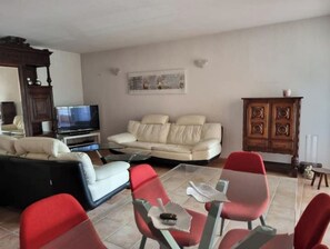Una sala de estar con un sofá, sillas rojas, un televisor y un mueble de madera.