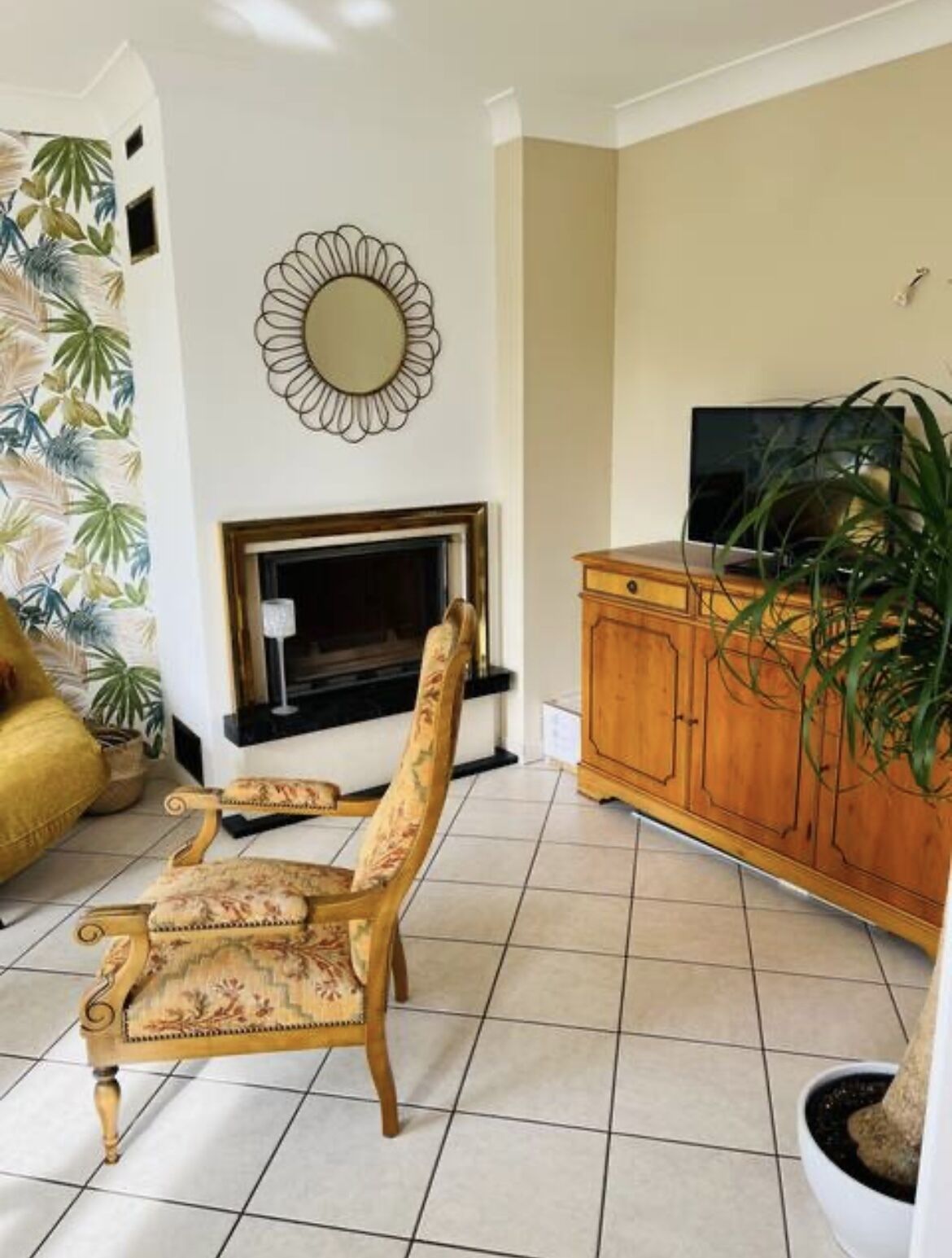 A living room with a fireplace, a television, a wooden cabinet, and a floral armchair.