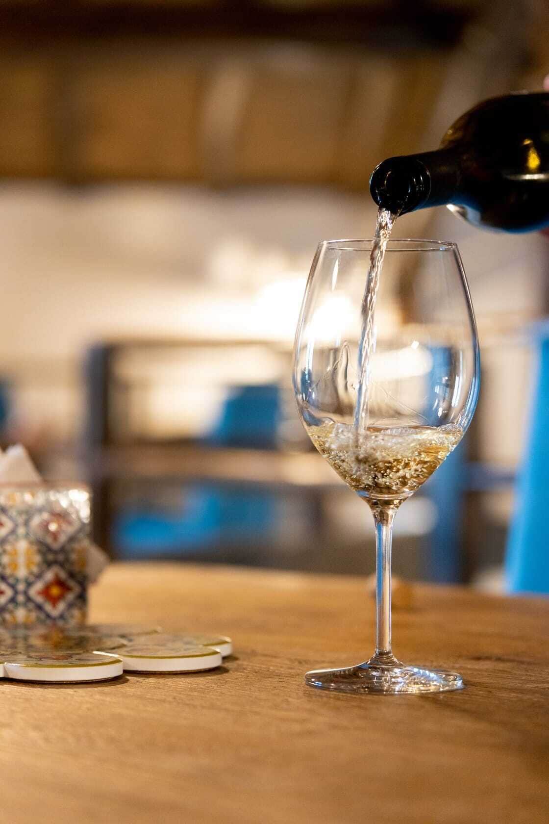 A glass being filled with a clear liquid, likely a beverage, on a wooden surface with patterned coasters.