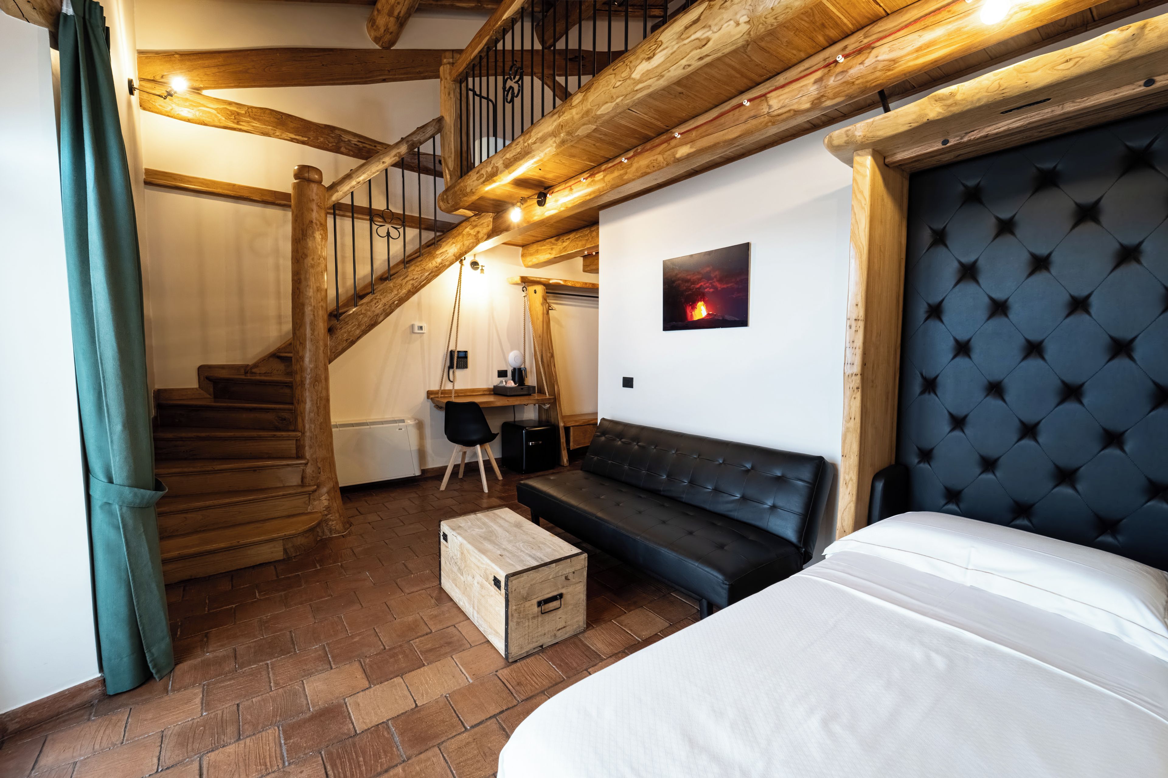 Una habitación con escalera de madera, sofá negro, cama y escritorio con silla.