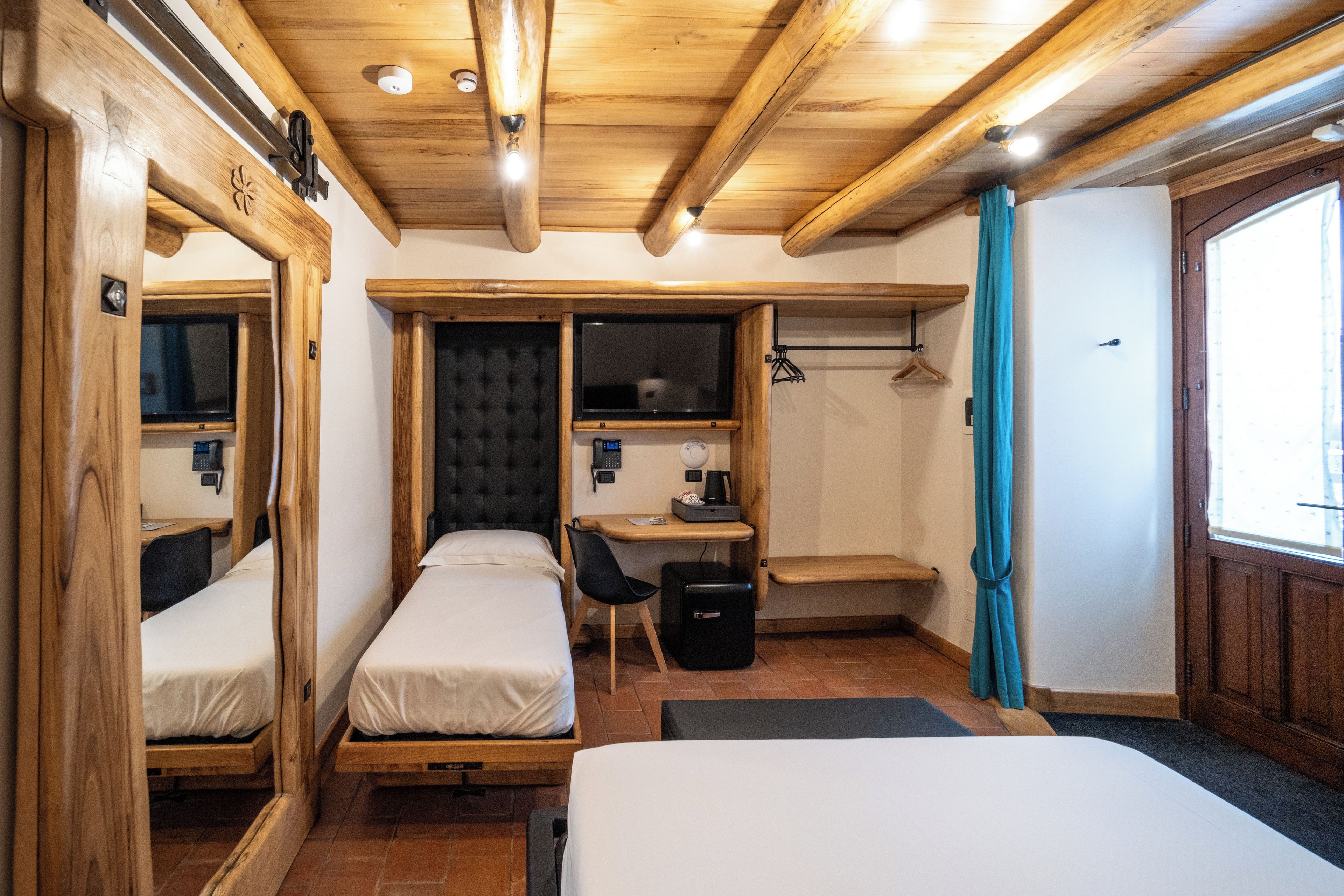 Une chambre d’hôtel compacte comprenant deux lits simples, un bureau, une chaise, une petite table et un miroir.
