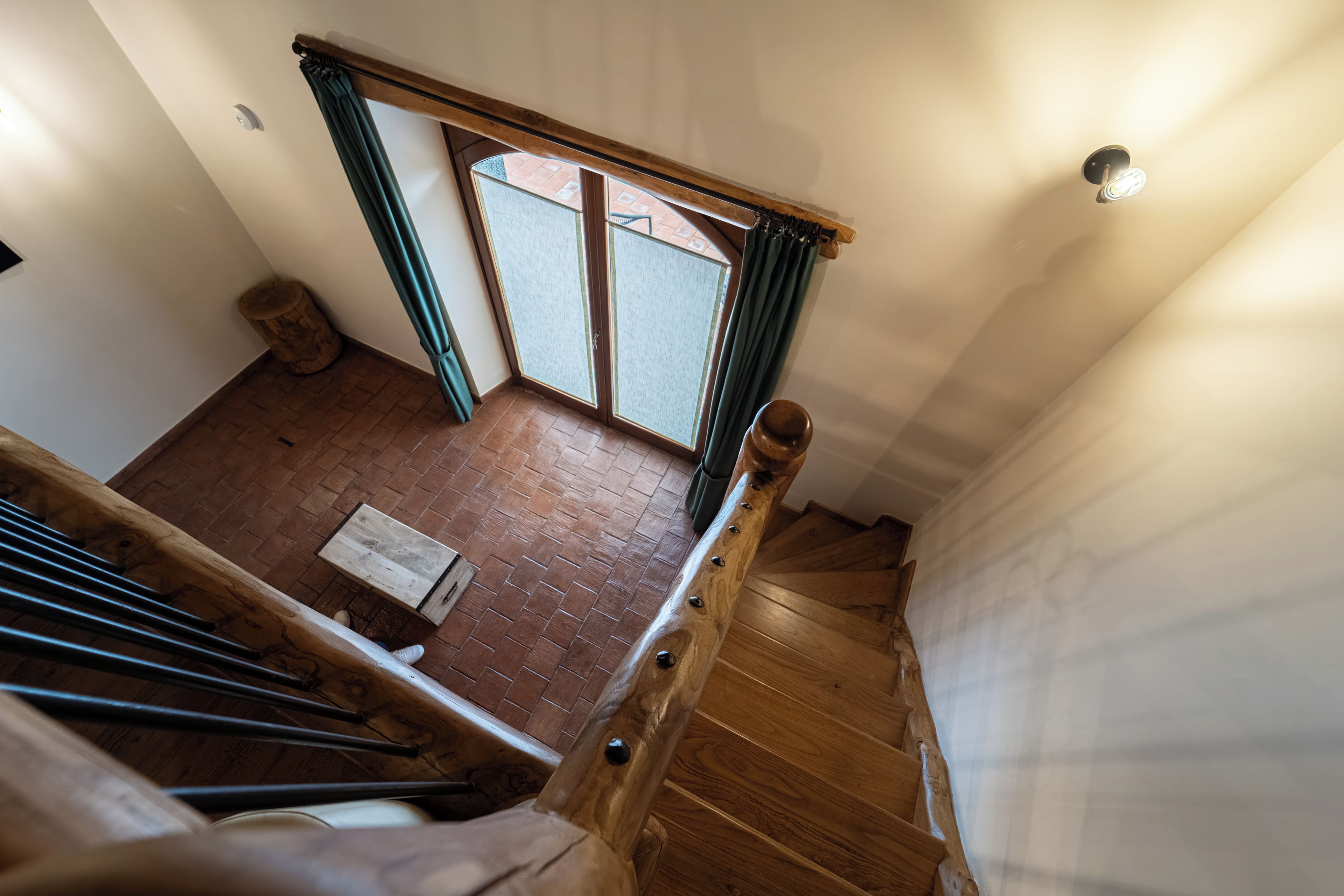 A wooden staircase with a view of a brick floor and a window with curtains.
