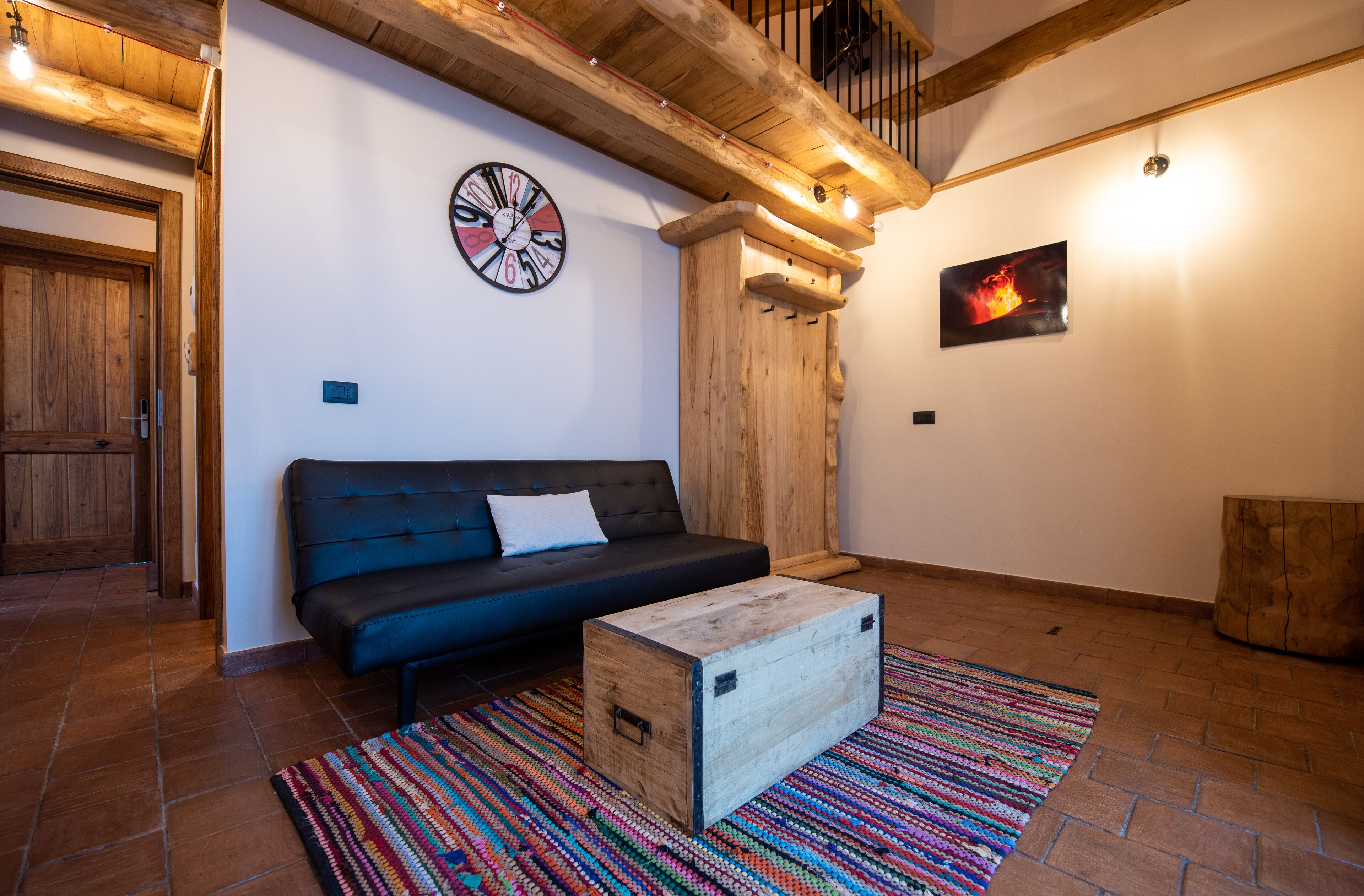 Un soggiorno accogliente con un divano blu scuro, un tavolino in legno, un tappeto colorato, una sveglia a muro in legno e un quadro incorniciato.