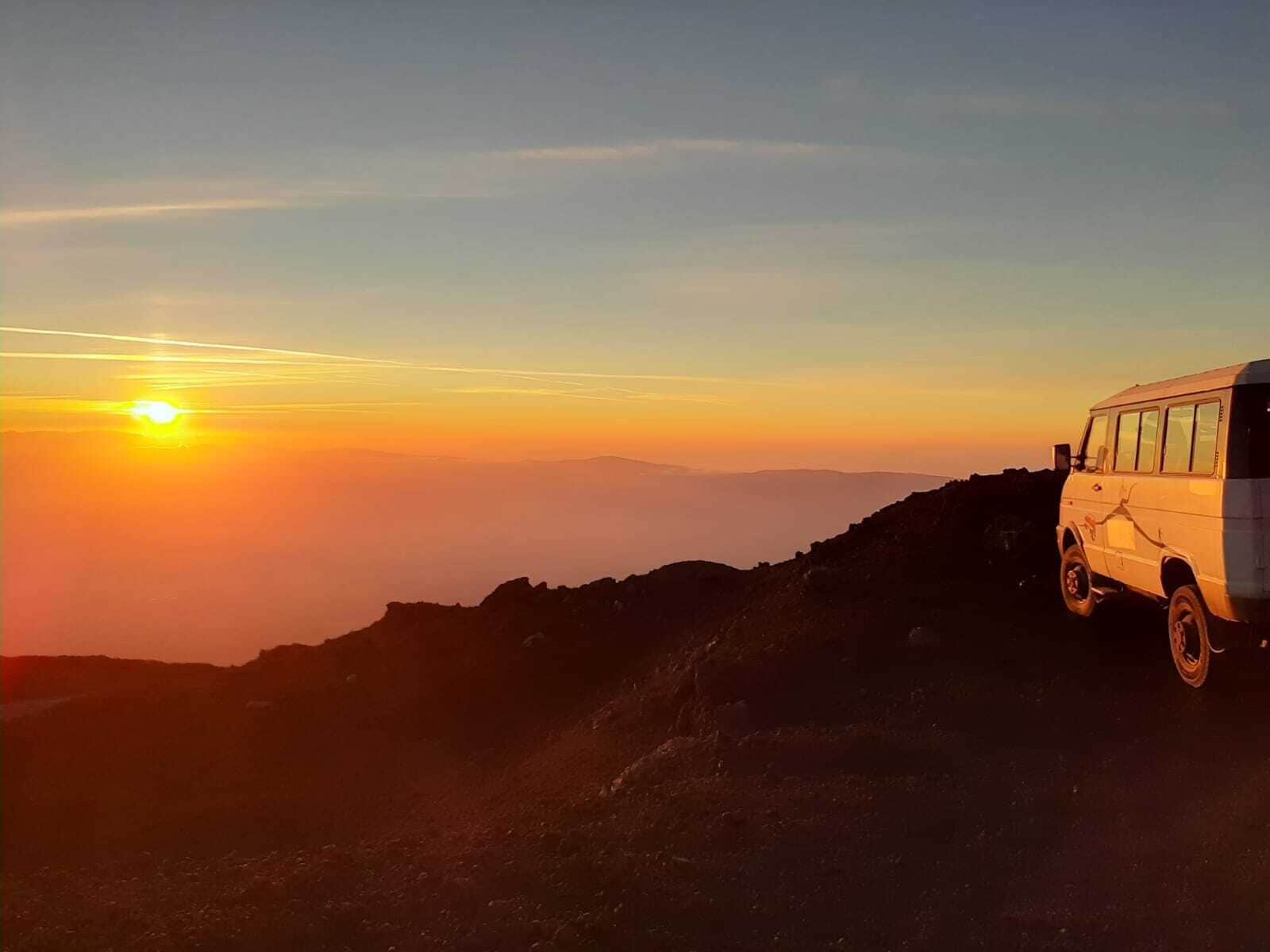 Un fourgon blanc est garé sur une crête montagneuse au coucher du soleil.