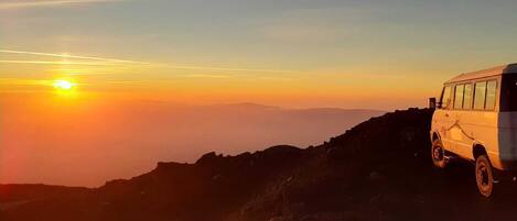 Un fourgon blanc est garé sur une crête montagneuse au coucher du soleil.