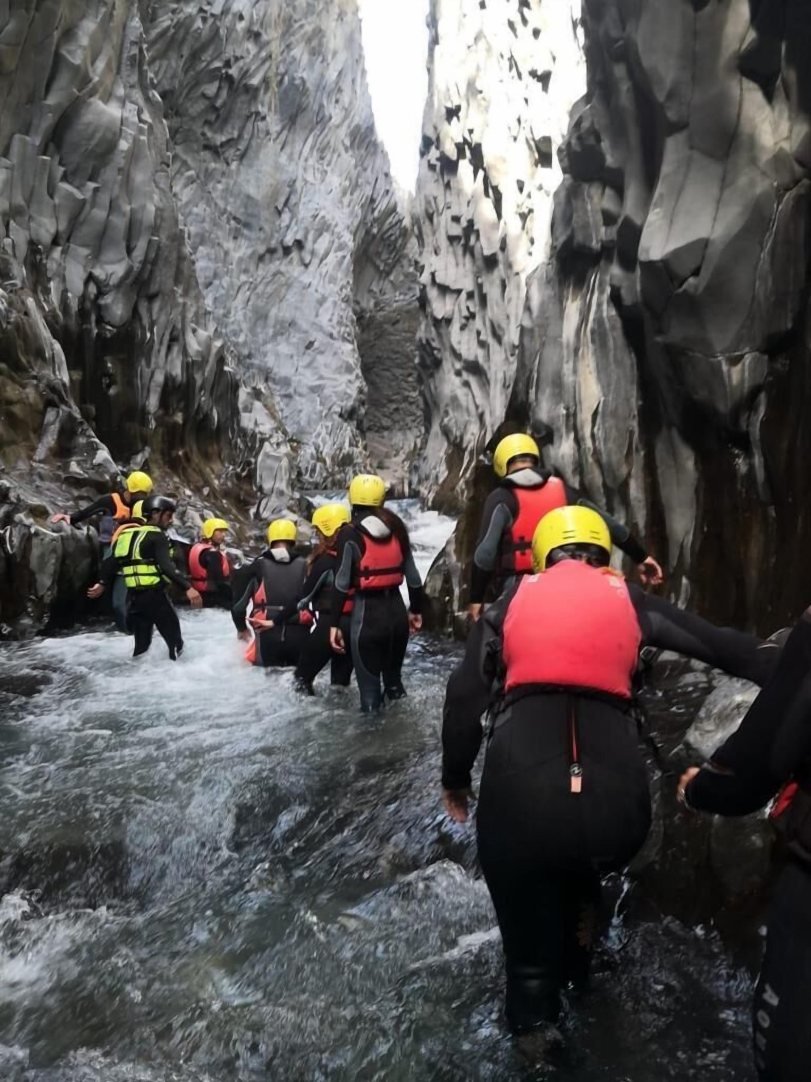 A group of people wearing helmets and life jackets navigating through a narrow, rocky water passage.