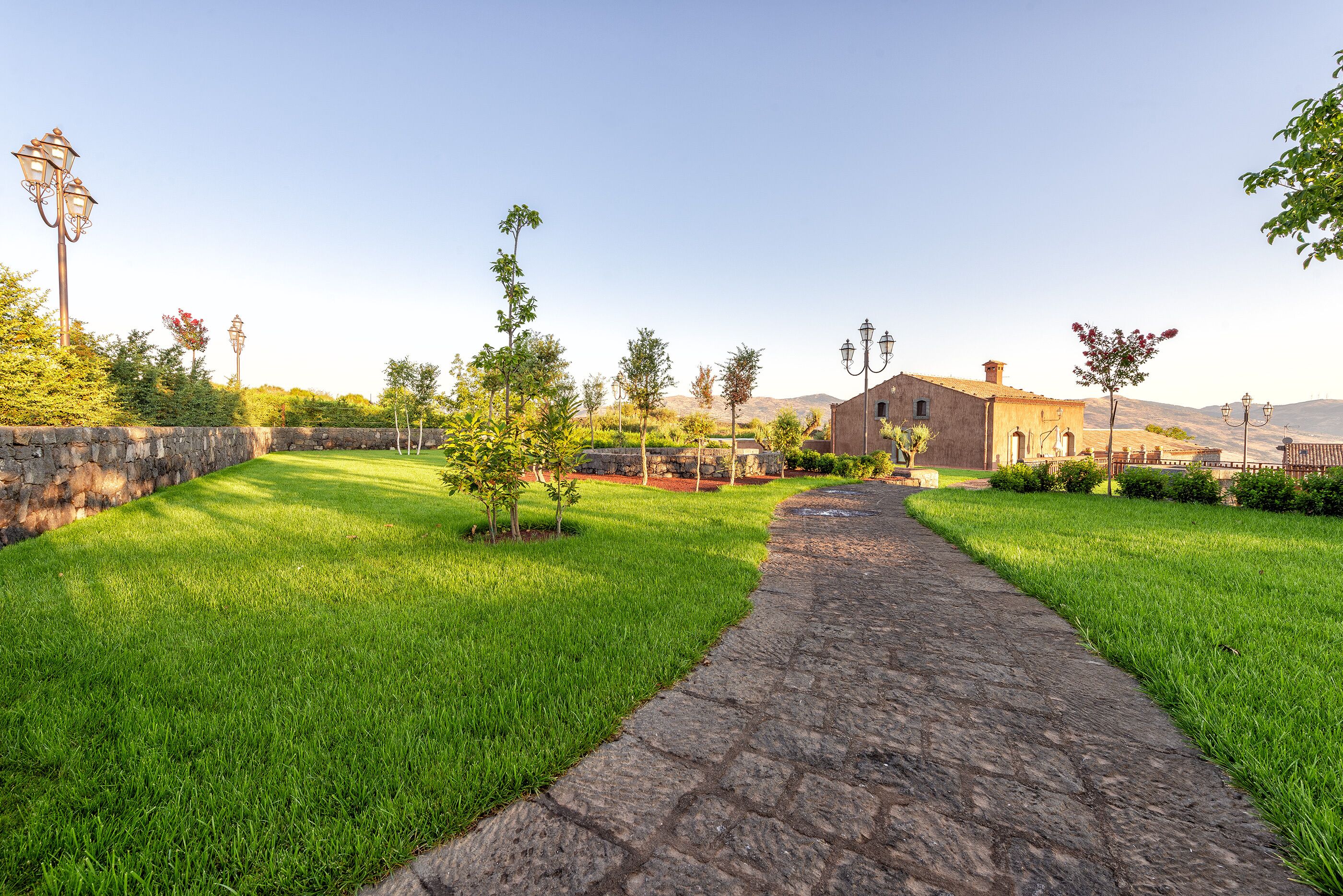 A stone pathway leading to a building with a stone wall and trees.
