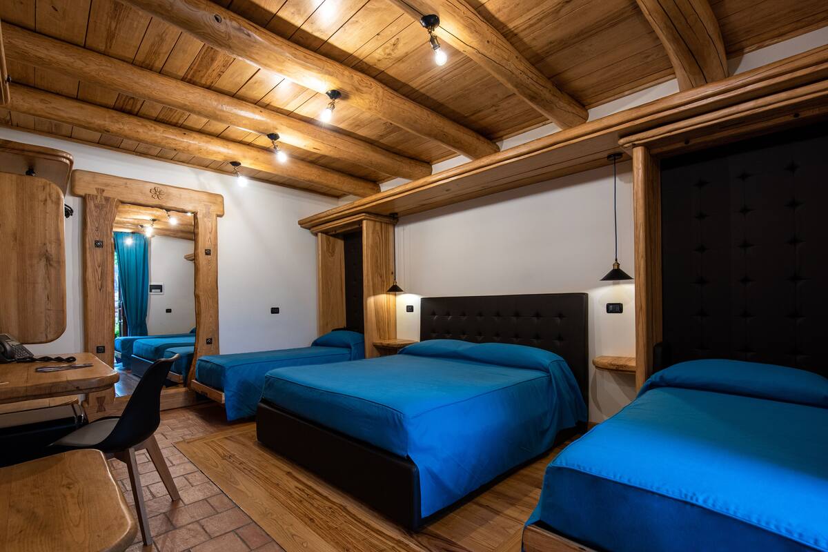 A room with wooden beams, a bed with a black headboard, a small table, and a chair.