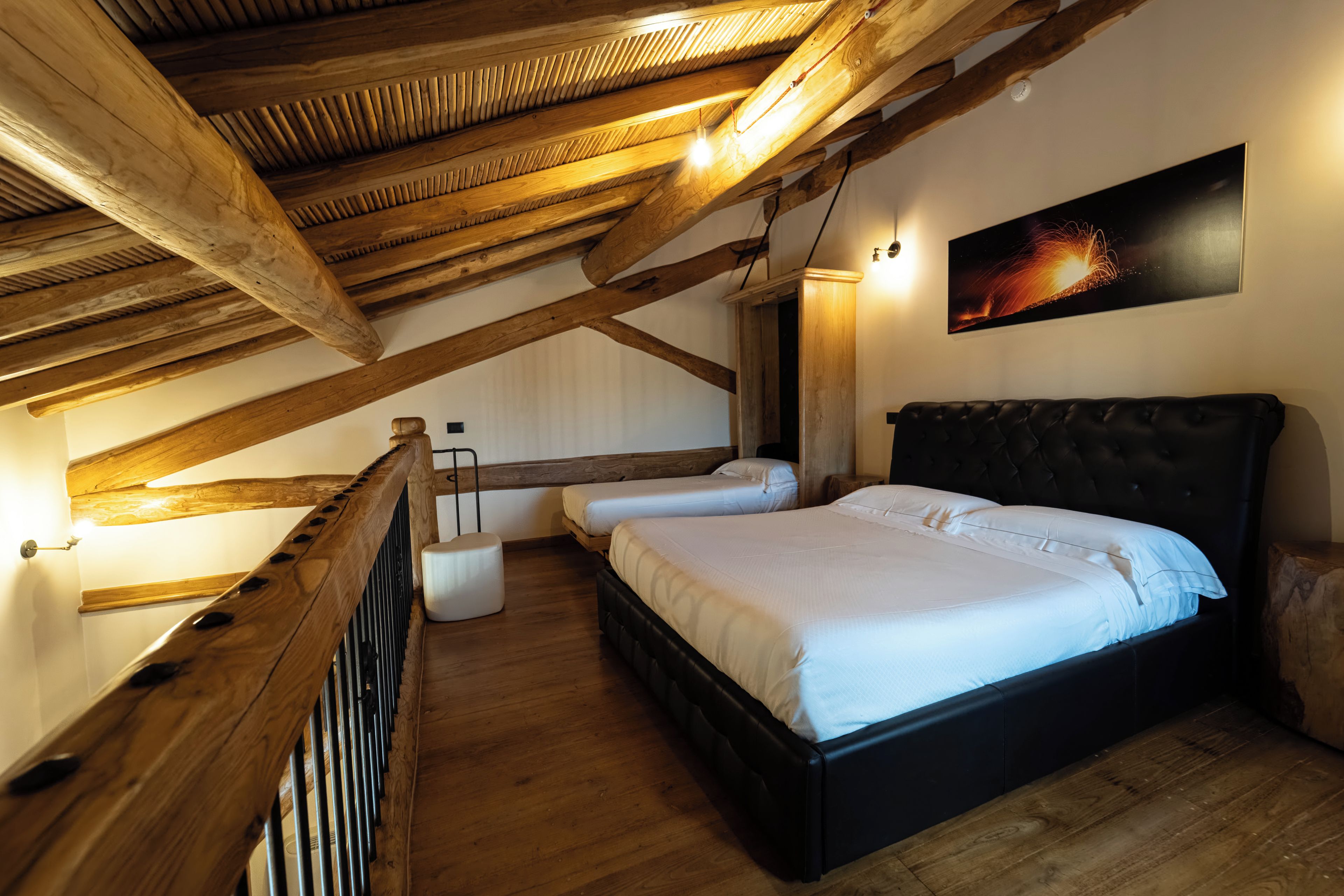 Ein Schlafzimmer mit schrägem Dach, Holzbalken, einem großen Bett, Nachttischen und einer wandmontierten Leuchte.