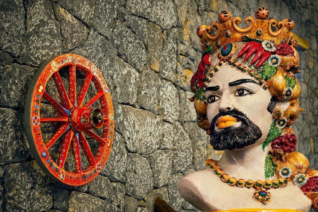 Eine Statue mit Krone und rotem Rad vor einer Steinmauer.
