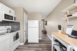 Une cuisine moderne avec des meubles blancs, un four à micro-ondes, une cuisinière et un réfrigérateur. On y trouve un plan de travail en bois, un bloc à couteaux et un évier.