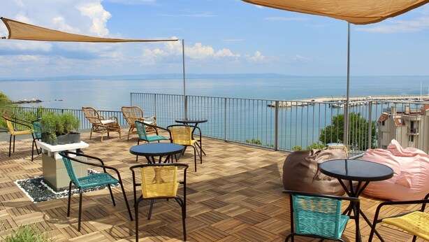 A terrace with outdoor furniture, a view of the sea, and a railing. - SUNSET ART HOTEL (Sozopol)