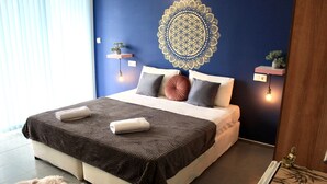 A modern bedroom with a large bed, a decorative wall hanging, bedside lamps, and a small plant on a shelf. - SUNSET ART HOTEL (Sozopol)