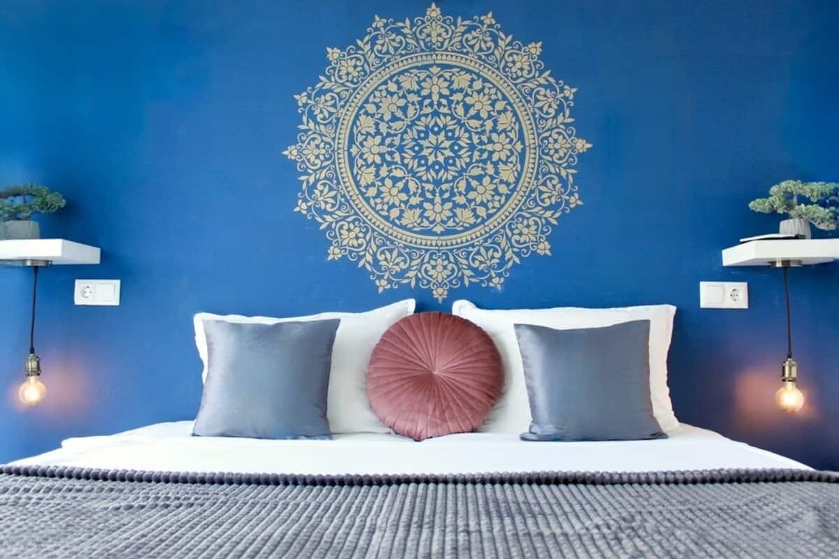 A bedroom with a blue wall, a decorative circular pattern, a bed with white and grey bedding, and two bedside tables with lamps.
