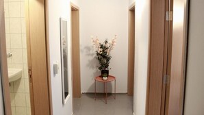 A narrow hallway with wooden doors on either side, a small round table with a potted plant, and a tiled floor. - SUNSET ART HOTEL (Sozopol)