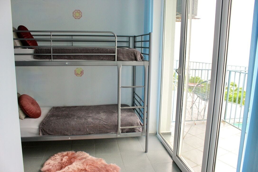 Ein Schlafsaalzimmer mit Etagenbetten, einem kleinen Teppich und einem Balkon mit Geländer.