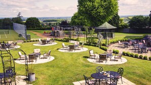 A well-maintained outdoor patio area with multiple seating arrangements, a children's play structure, and a gazebo. - Blunsdon House Hotel (Swindon)