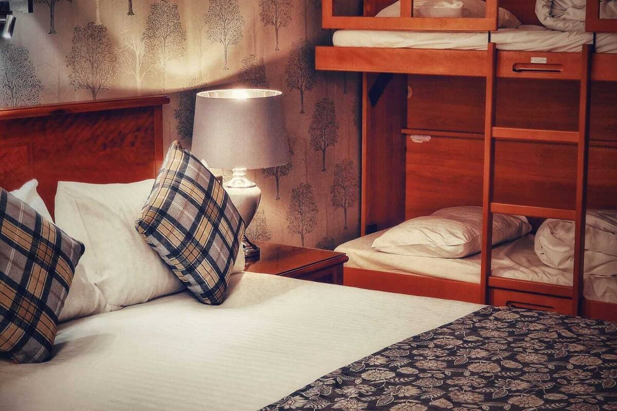 A bunk bed with a wooden frame, a bedside table with a lamp, and a patterned bedspread.