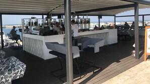 En udendørs bar med havudsigt, med en bardisk, barstole, grill og et udvalg af flasker og glas.