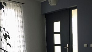 Et rum med en mørk dør, et hvidt gardin med cirkulære mønstre, en hængende lysarmatur og et flisegulv.