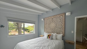 Quarto com uma cama grande, janela com vista, cabeceira decorativa e porta que dá para outro cômodo.