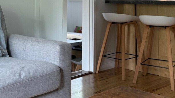 Uma cozinha moderna com banquetas de madeira, bancada branca e vista para uma sala de jantar.