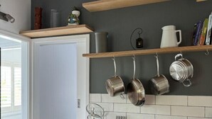 Cozinha moderna com armários de madeira, bancada preta, panelas penduradas e painel de azulejos brancos.