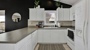 A modern kitchen with white cabinetry, a black accent wall, a coffee machine, and a refrigerator.