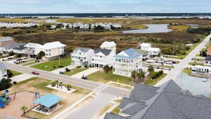 A coastal residential area with multiple white two-story houses, a playground, and a road leading to the beach.