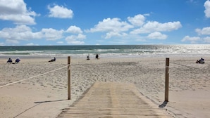 A beach with a wooden boardwalk leading to the water, people sitting and walking along the shore.