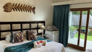 A bedroom with a large bed, a wooden fish wall decoration, a ceiling fan, and a view of the outdoors through a glass door. - Whalesong guest house (St. Lucia)