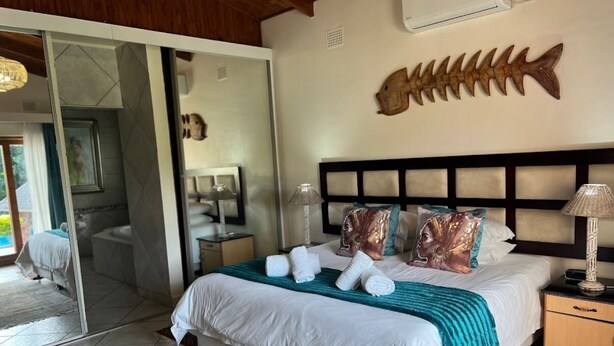 A hotel room with a bed, a nightstand, a lamp, a fish-shaped wall decoration, and a sliding glass door leading to a bathroom. - Whalesong guest house (St. Lucia)