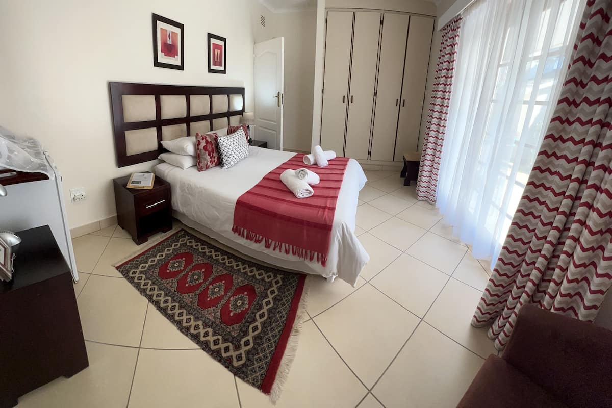 Quarto de hotel com cama, mesa de cabeceira, armário e janela com cortinas.
