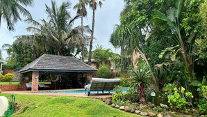 A poolside area with a covered seating area, a brick building, and lush tropical vegetation. - Whalesong guest house (St. Lucia)