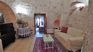 A cozy living room with a stone wall, a sofa, a small table, a lamp, and a TV on a cabinet. - CASA CICCONE CARDONE , trulli with Jacuzzi  and private parking lot  (Locorotondo)